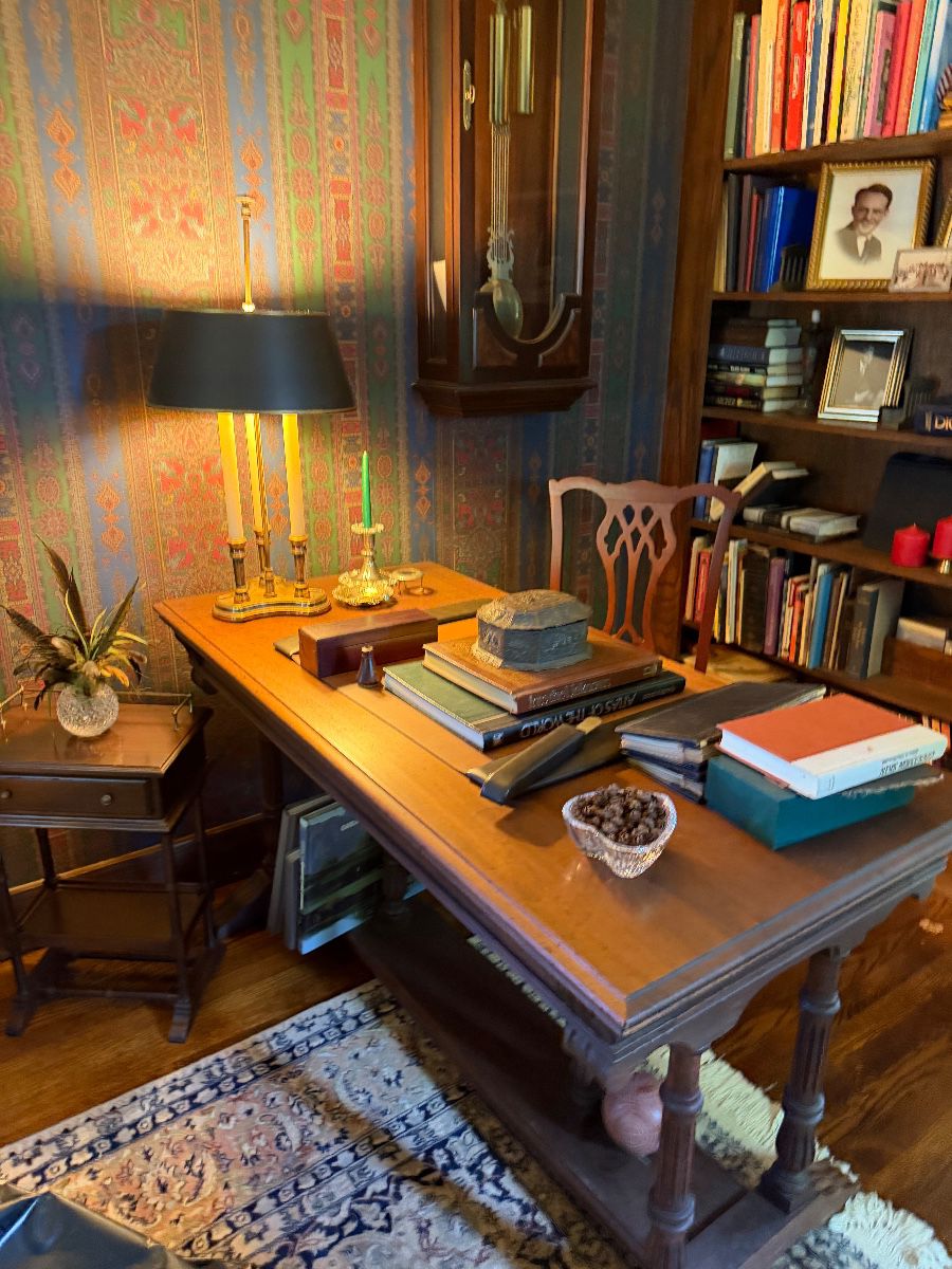 Furnished study with a wooden table, grandfather clock, books, and collectibles at the Caldwell estate sale
